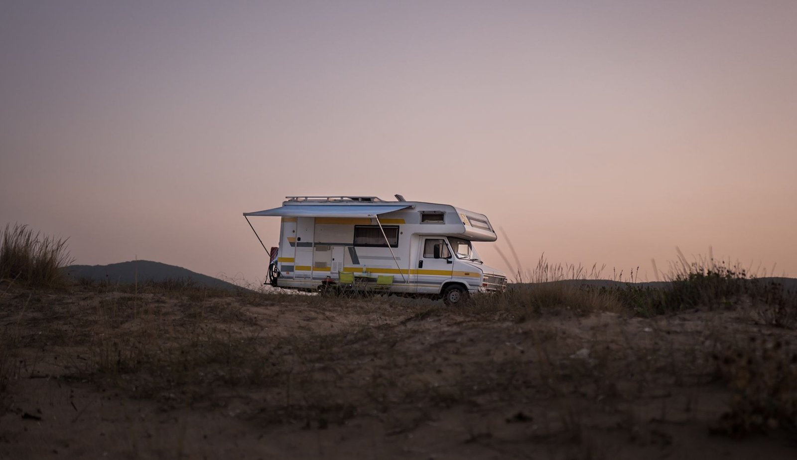 A motorhome parked among dunes at sunset